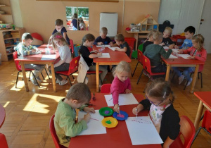 dzieci przy czterech stolikach maluja fioletową farbą kropki patyczkiem do uszu
